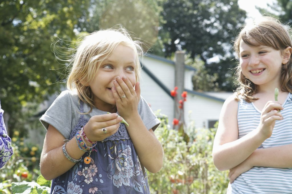 Two children standing outdoors in a garden laughing.