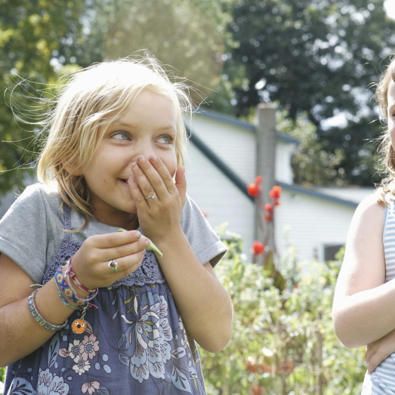 Two children standing outdoors in a garden laughing.